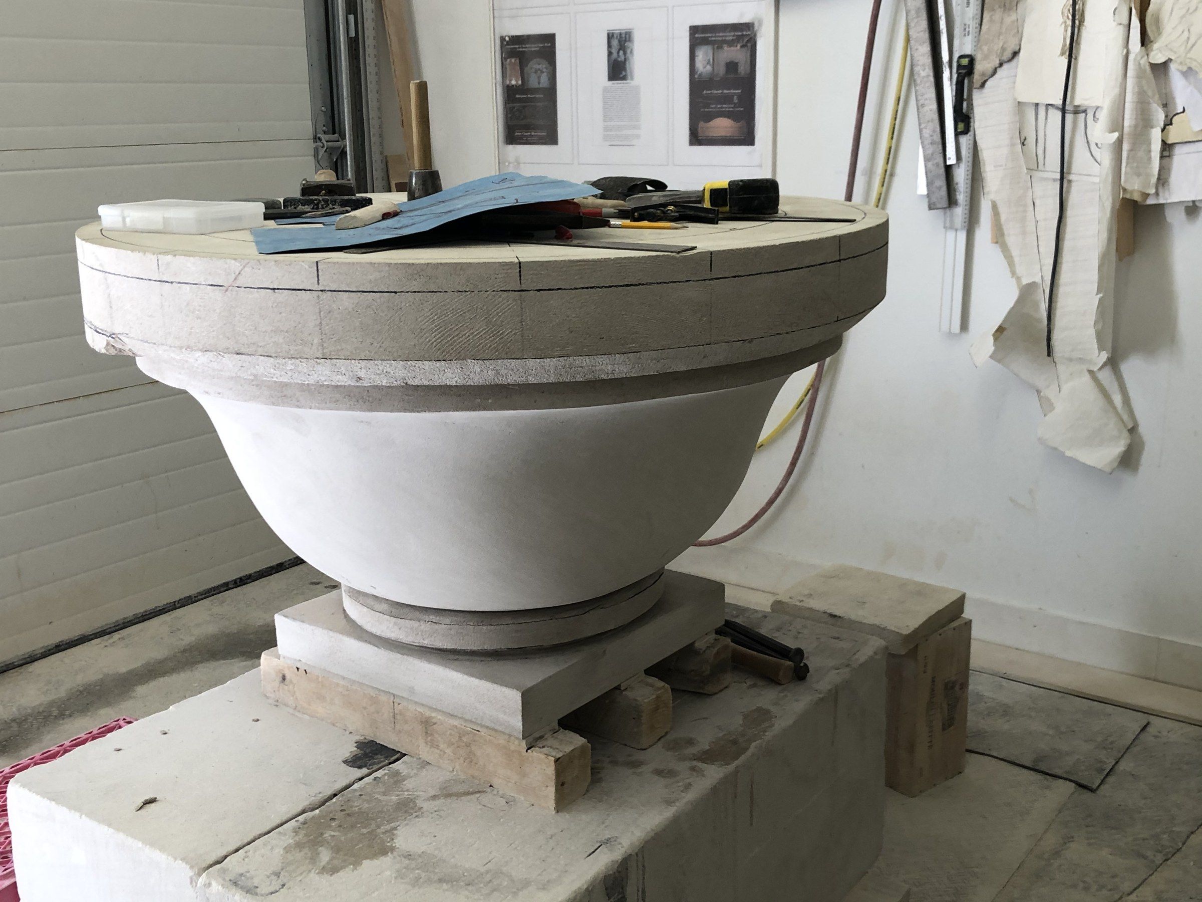 The outside of the fire pit smoothed into a clean curve between the rim band and a round foot, with tools and templates laid on top.