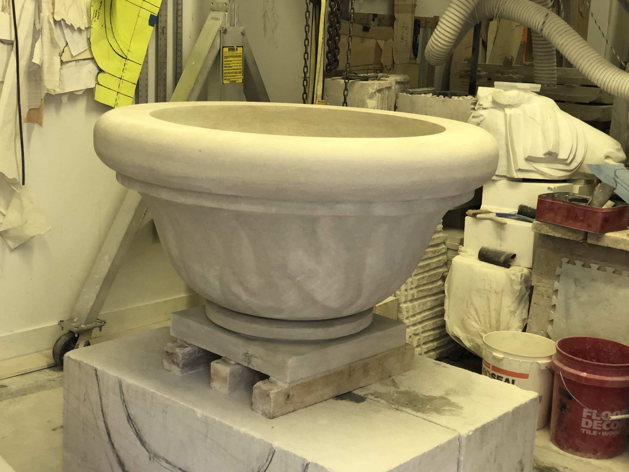 The finished fire pit on its plinth in the studio: a rolled rim over a smooth body, set on a round foot.