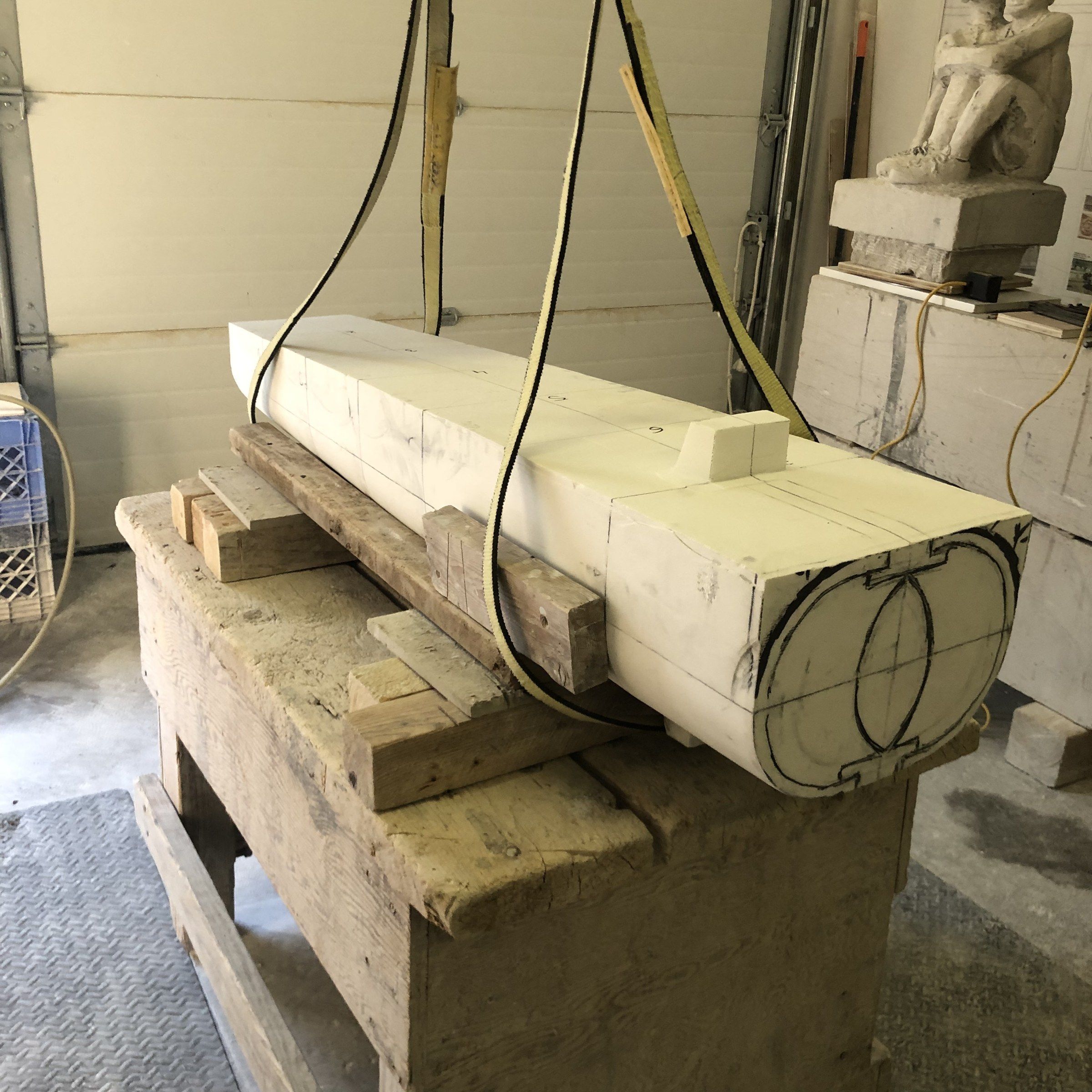 November 2024: the marble block on a workbench in lifting straps, squared, with two overlapping circles drawn on its end to mark the form.
