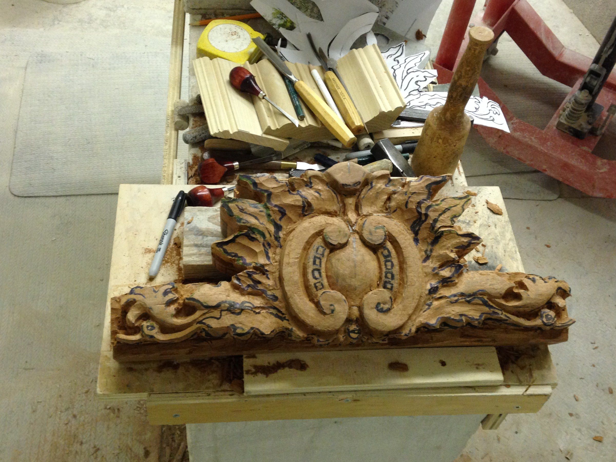 The cartouche being carved, its outlines drawn in marker, among gouges, a mallet and paper templates.