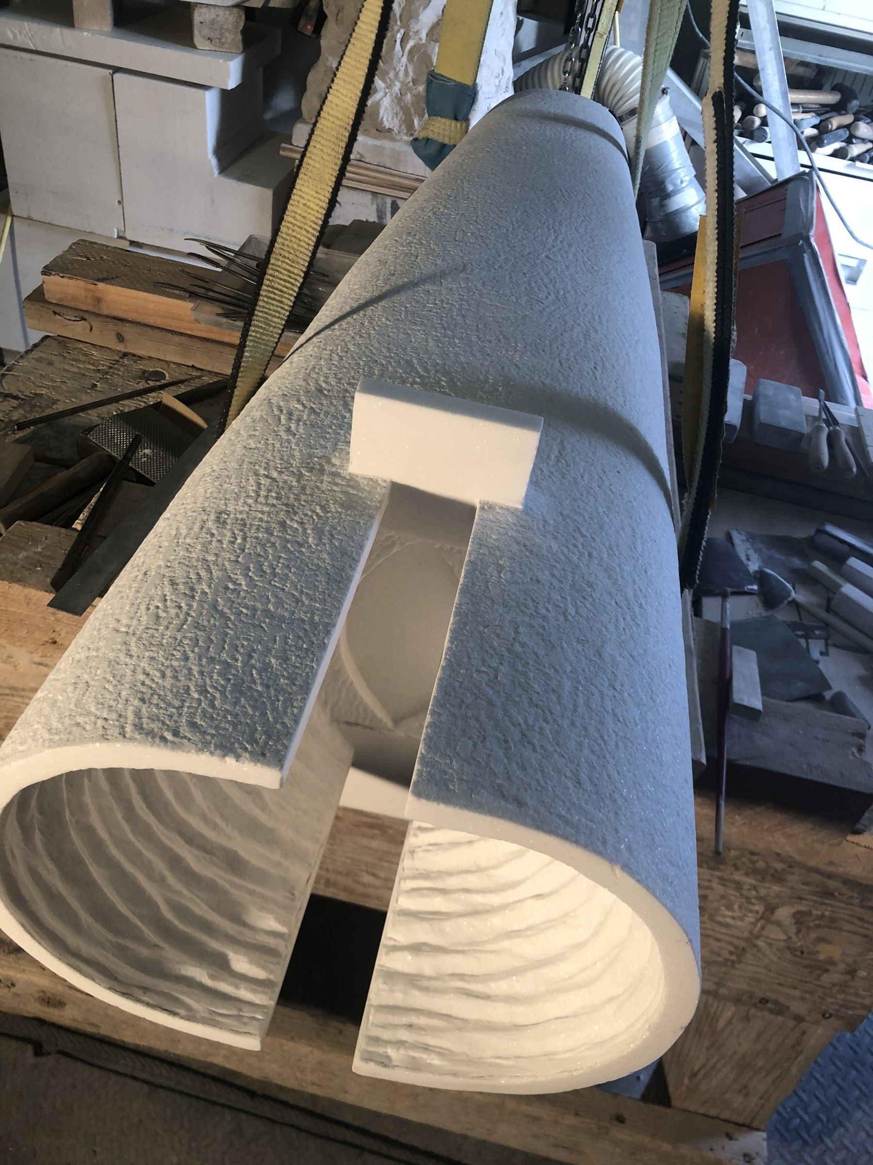 March 2025, in the studio: the marble lying on its side in lifting straps, the inside of the cylinder hollowed, with chisel ridges still visible, and a slot cut through the wall.