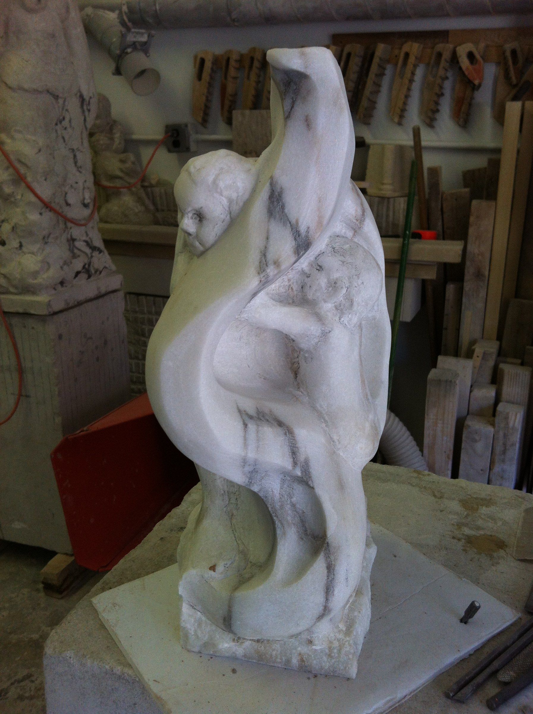 The sculpture seen from the side: the child's head and the sweeping curve of the marble, its grey veins running through the form.