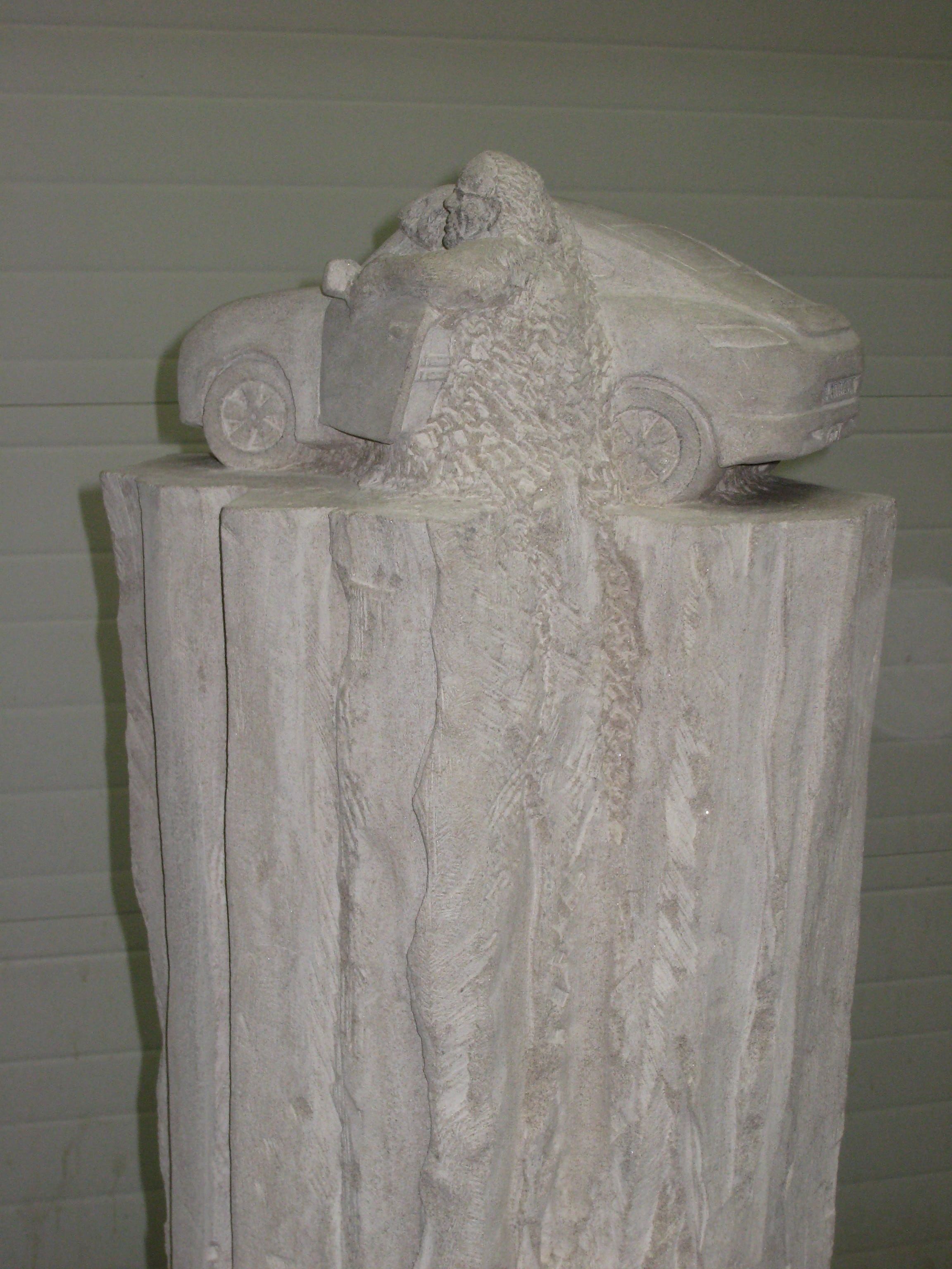 Detail of the stone sports car with a carved figure emerging from the body of the vehicle, hand-carved in the same limestone block.