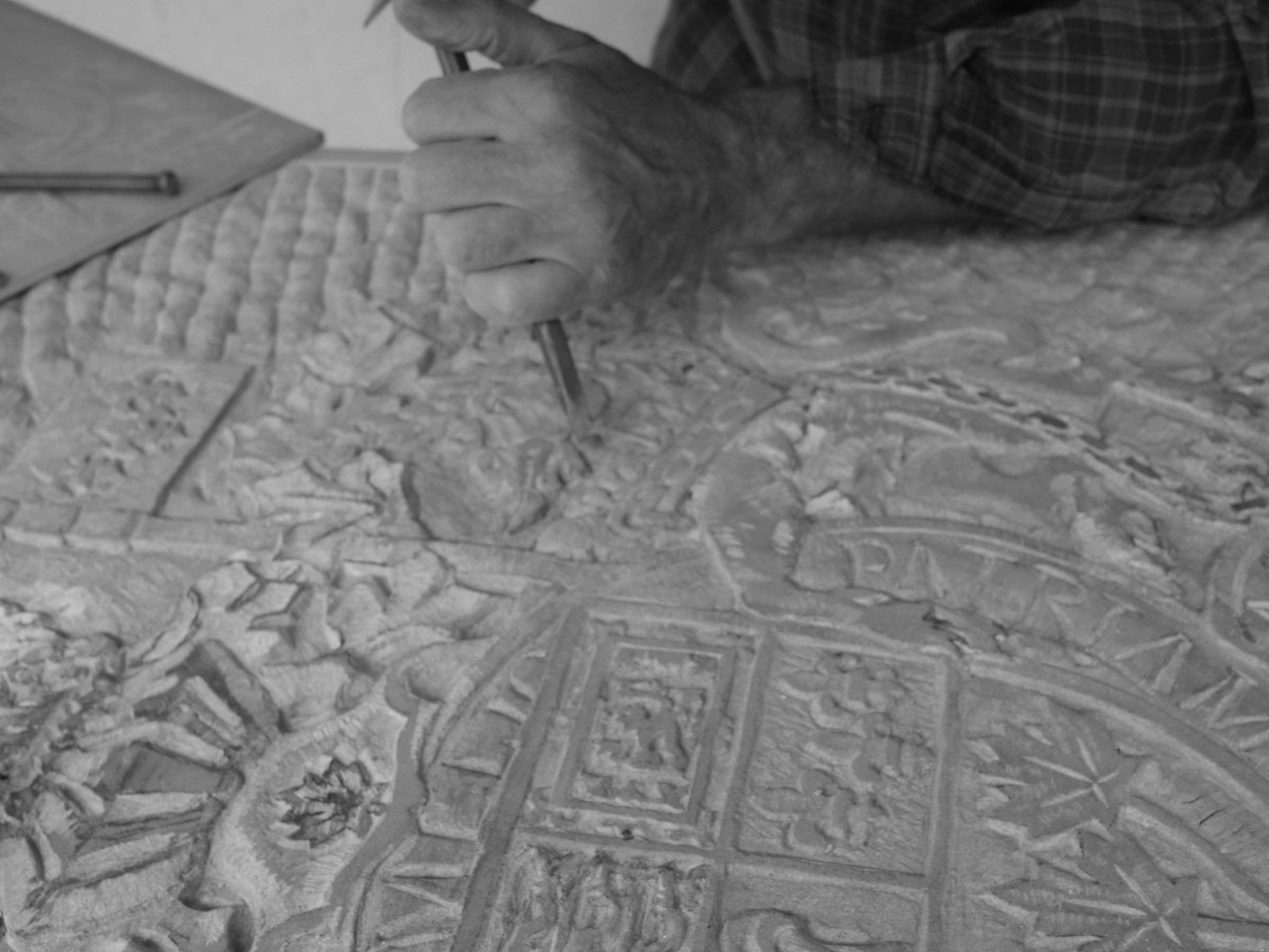Close-up of Jean-Claude Marchionni’s hands guiding a chisel across the relief: rosettes, tracery and small framed panels cut into the stone. Black-and-white photograph.