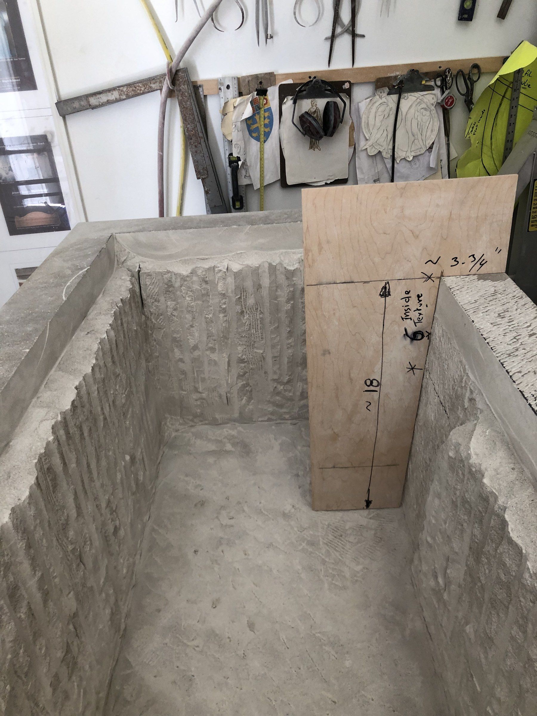 The interior being hollowed, its walls still ridged with chisel marks, a plywood template marked with measurements standing inside.