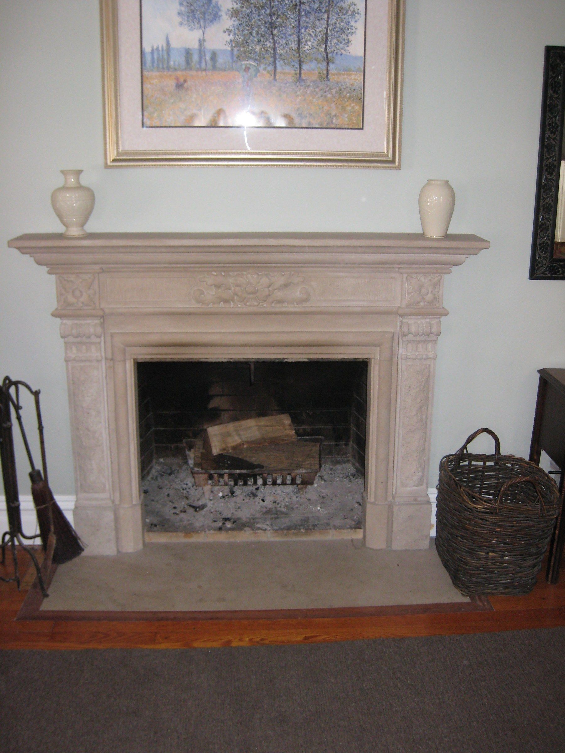 A limestone mantel with its frieze and pilasters carved with flowers and garlands, two vases on its shelf and a framed painting above.