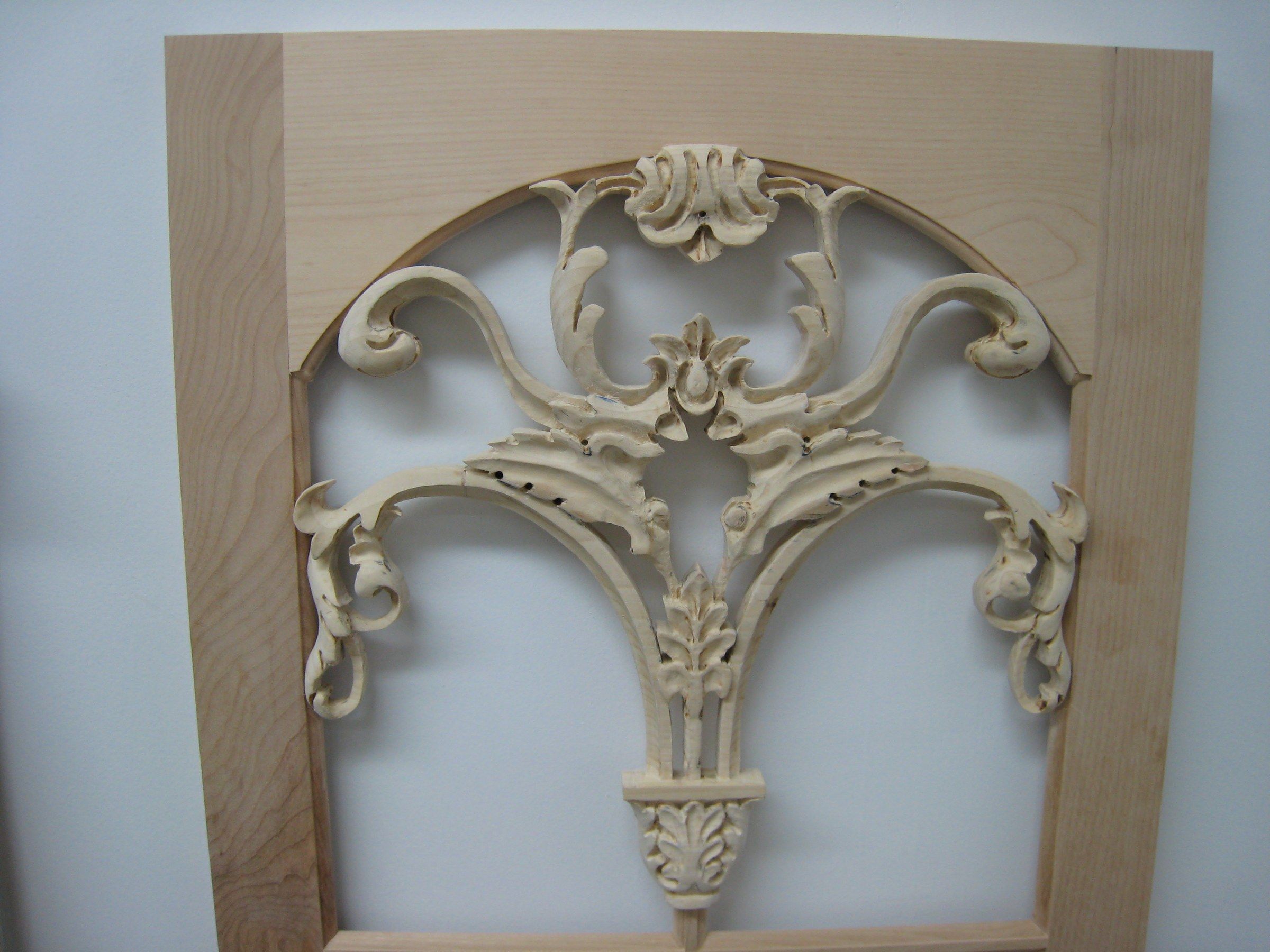 An arched maple frame holding an openwork carving: scrolls and acanthus leaves rising from a small leafy base to a shell-like crest.