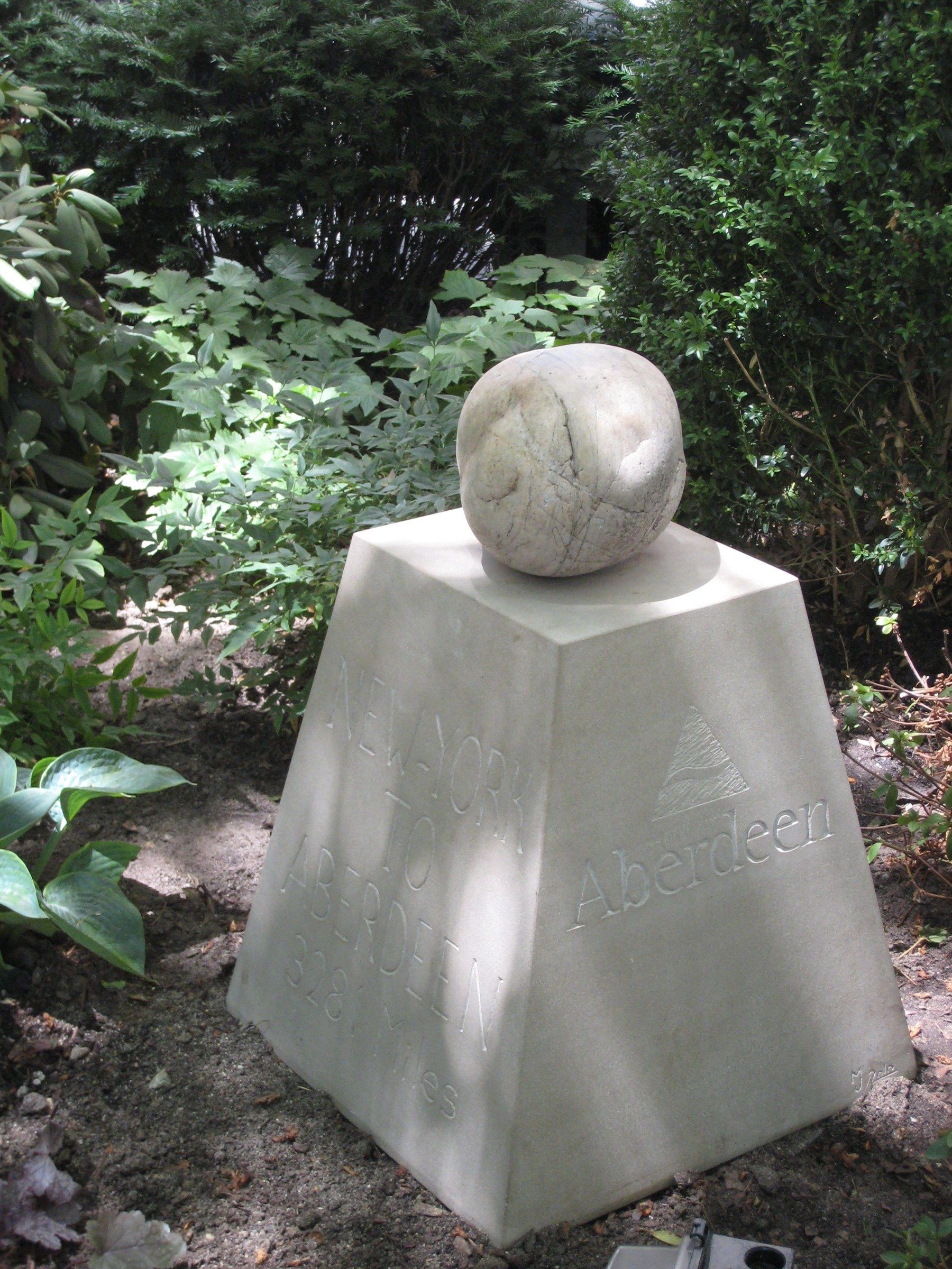The marker in dappled shade in the garden, both carved faces visible.