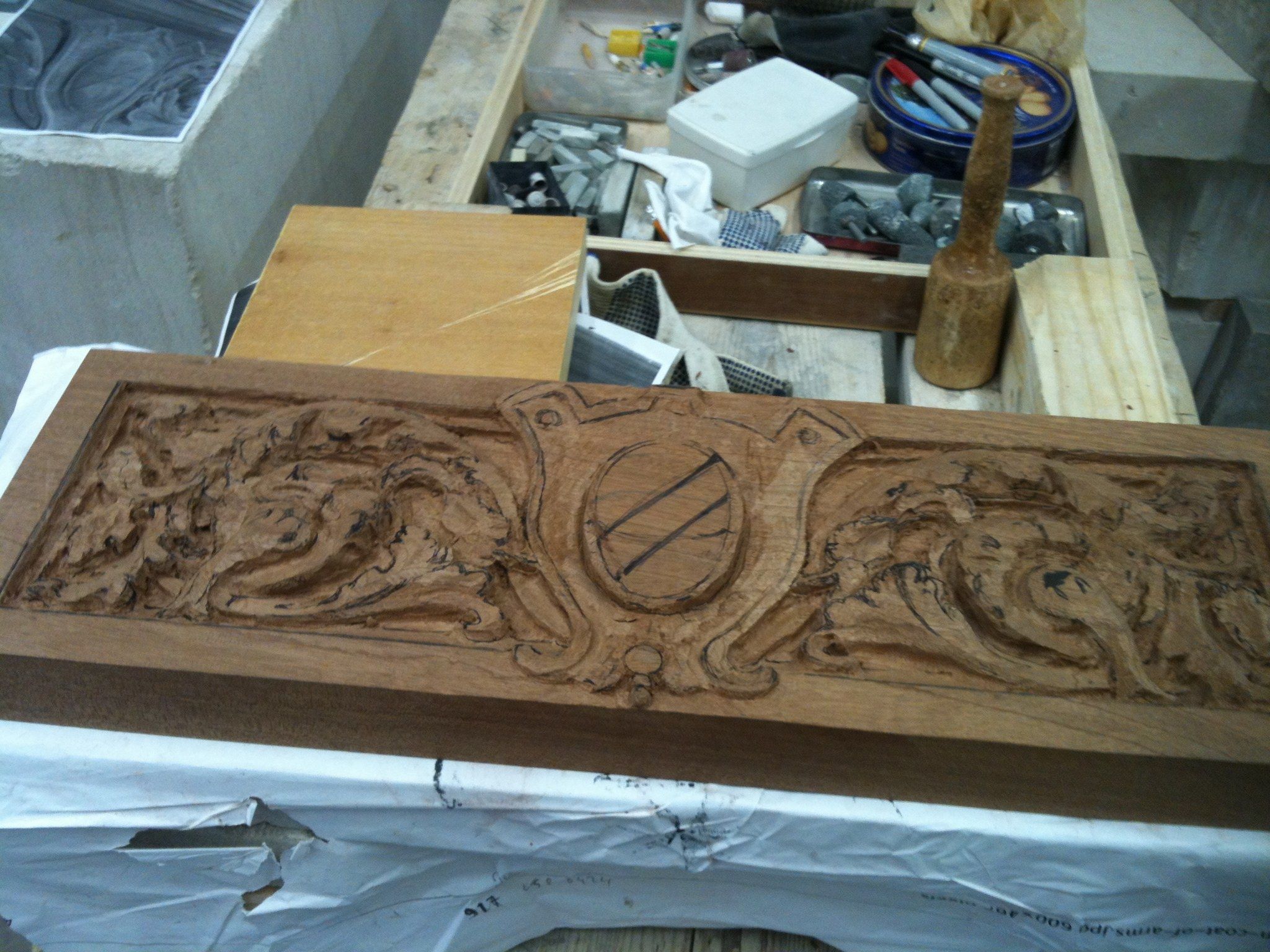 The panel with the acanthus scrolls roughed out on both sides of the cartouche, a mallet and tools on the bench behind.