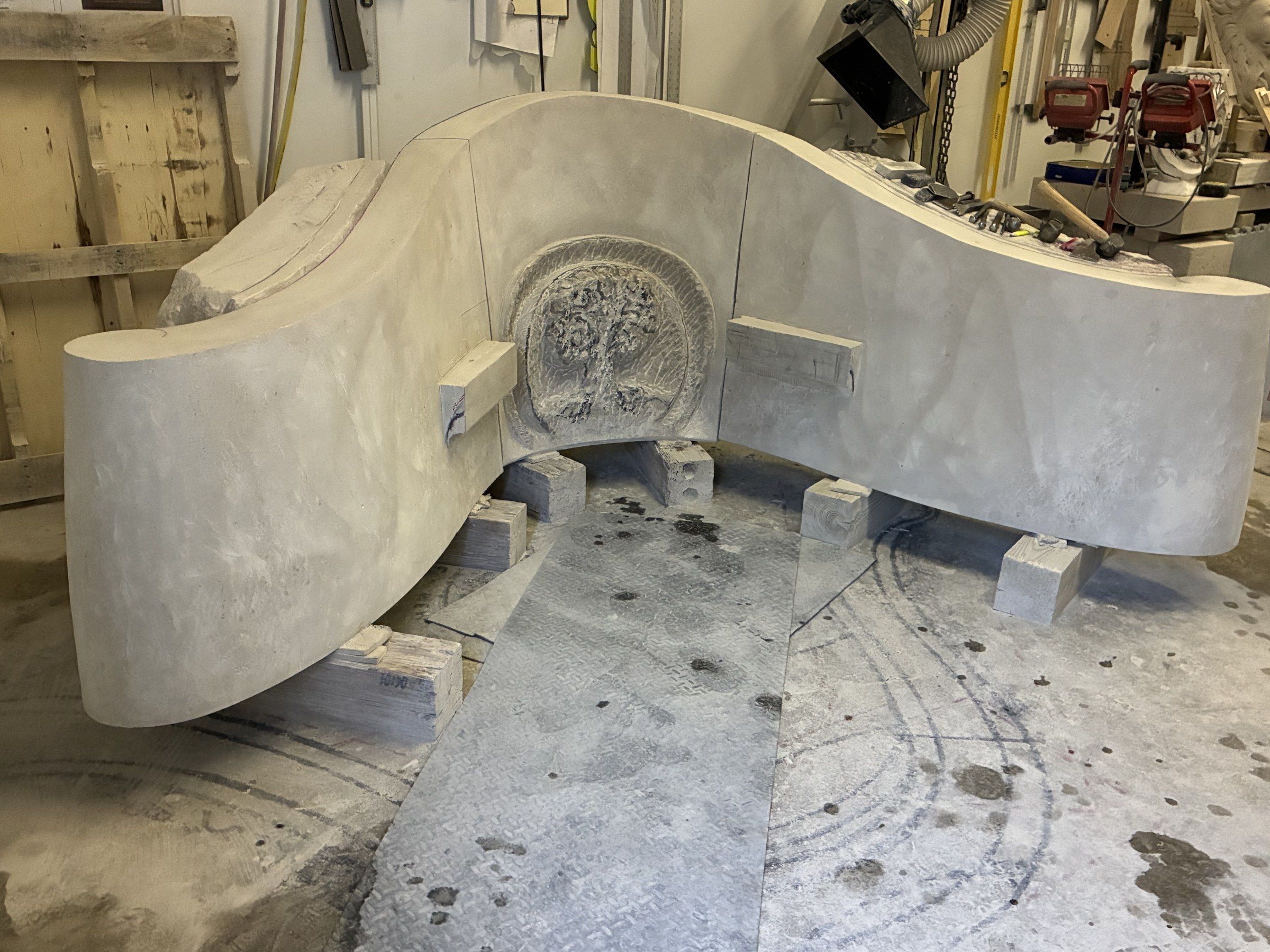 The three blocks assembled for the first time in April 2026, roughed out — central panel flanked by the two curved wings, with the circular medallion emerging in low relief.