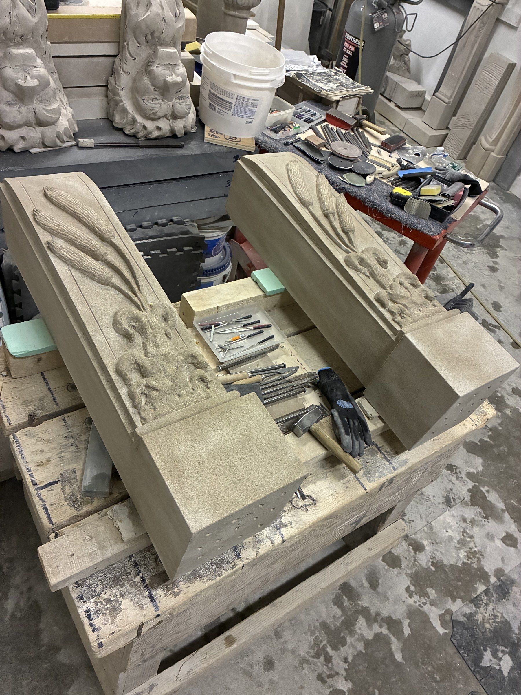 September 2025: the two finished jambs on a pallet, carved with ears of grain rising from a floral base, among carving tools.