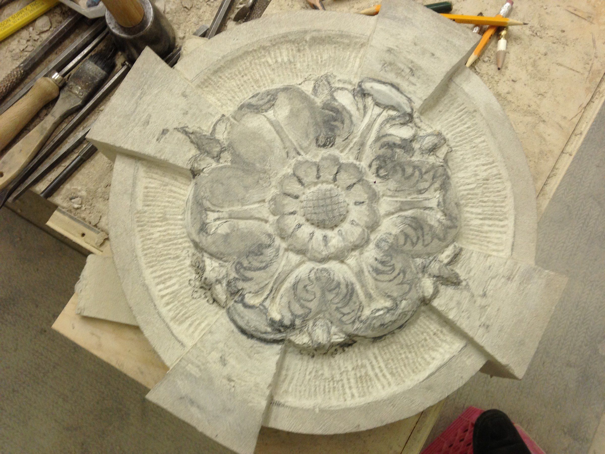 A rosette on the workbench: a layered flower framed by curling leaves, among chisels and pencils.