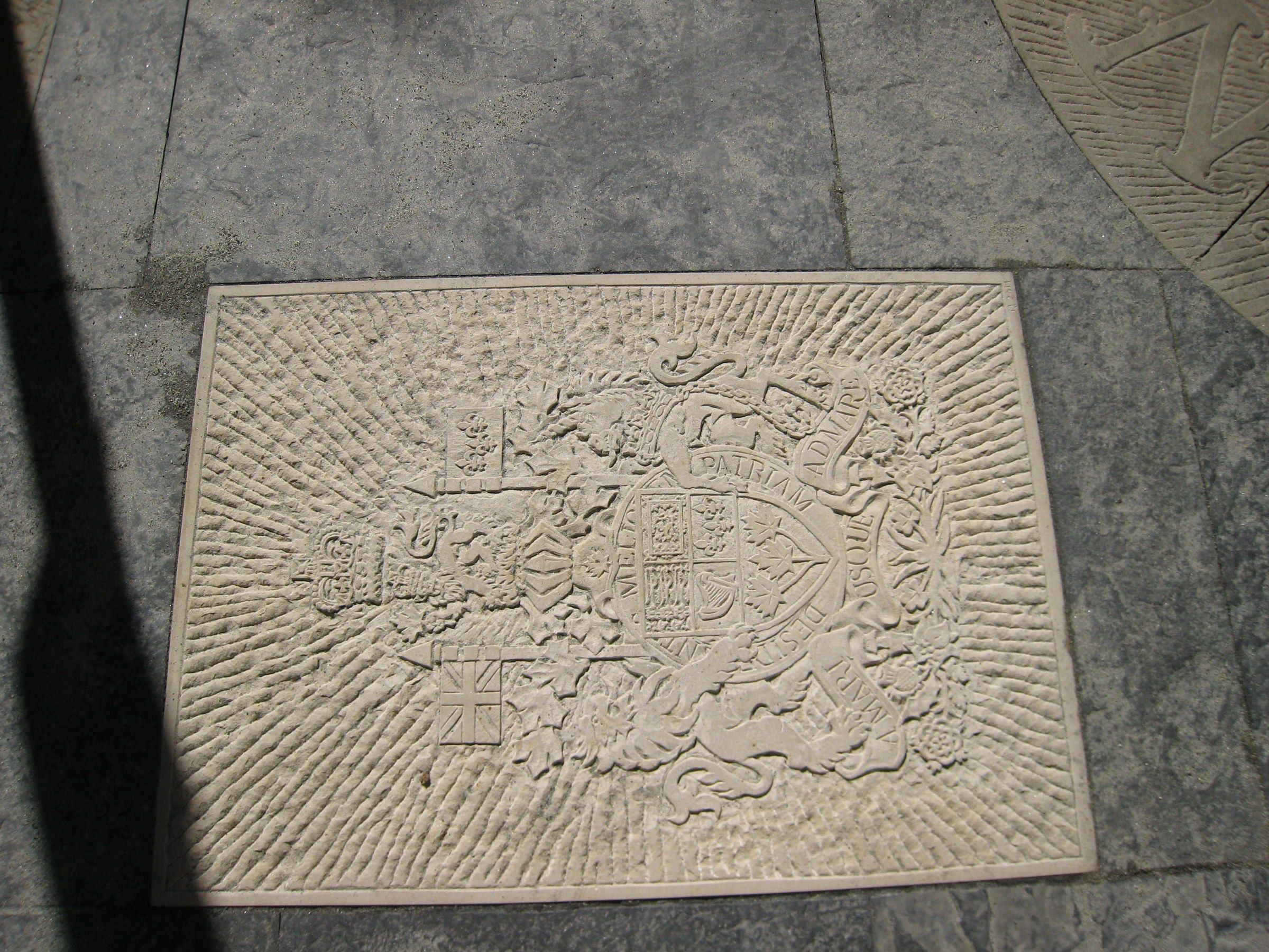 The relief set flush into the stone paving of the garden, half in sunlight and half in shadow, beside the edge of another carved stone.