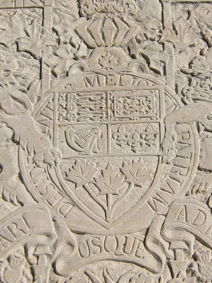 Close-up of the shield — three lions, a lion rampant, a harp, fleurs-de-lis and three maple leaves — inside a ring reading “DESIDERANTES MELIOREM PATRIAM.”