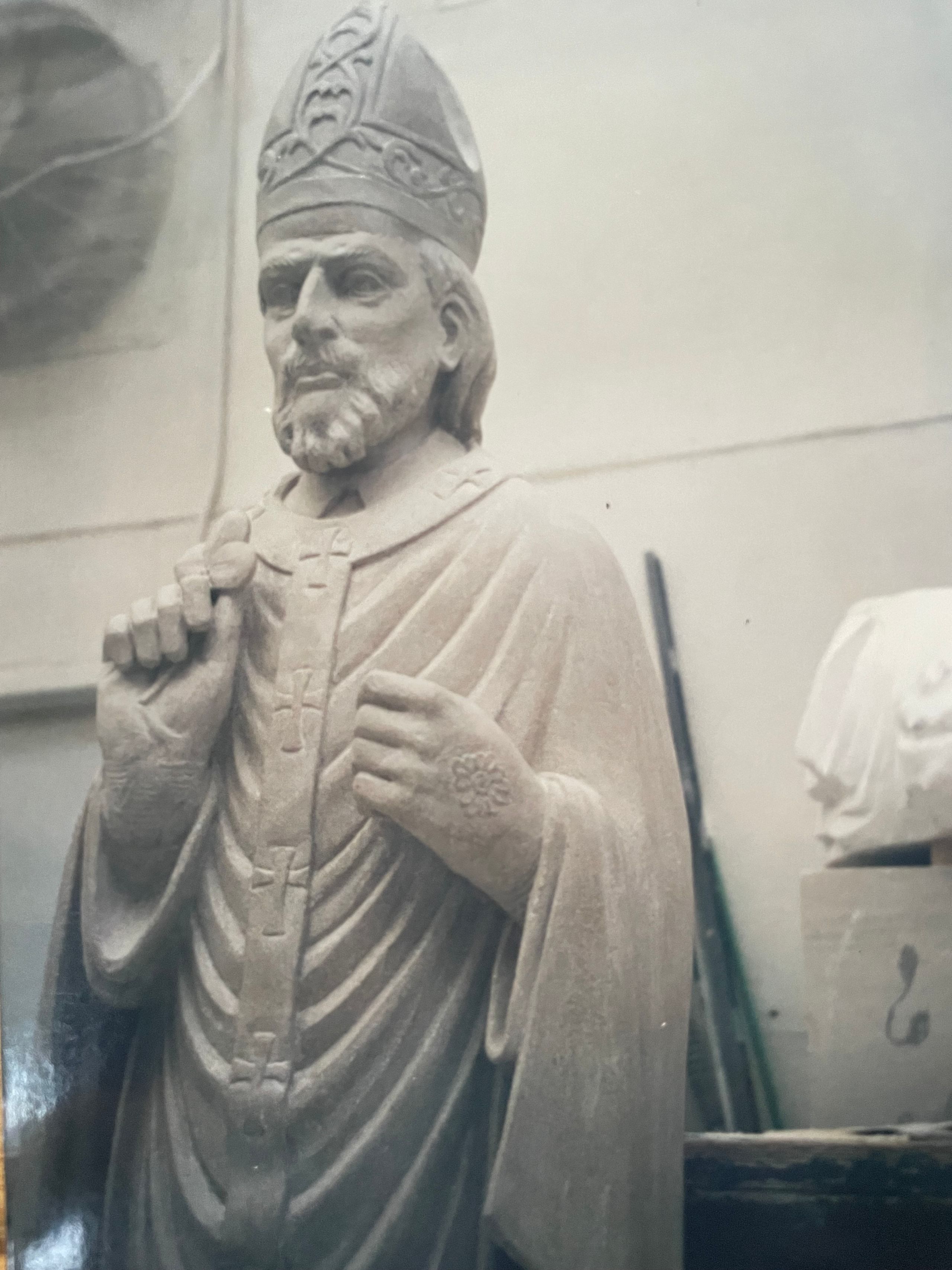 Carved limestone statue of a bishop wearing a mitre and vestments with crosses, standing in the workshop.