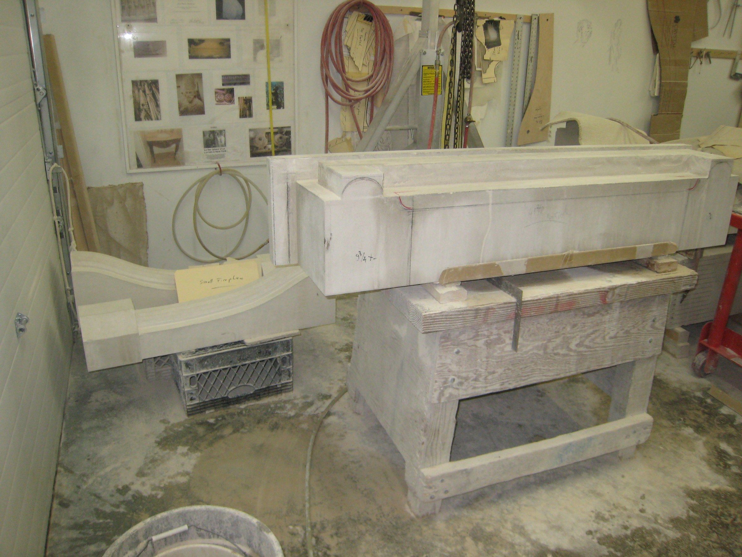 Limestone fireplace elements — mantel and curved surround — laid out on workshop benches before installation.